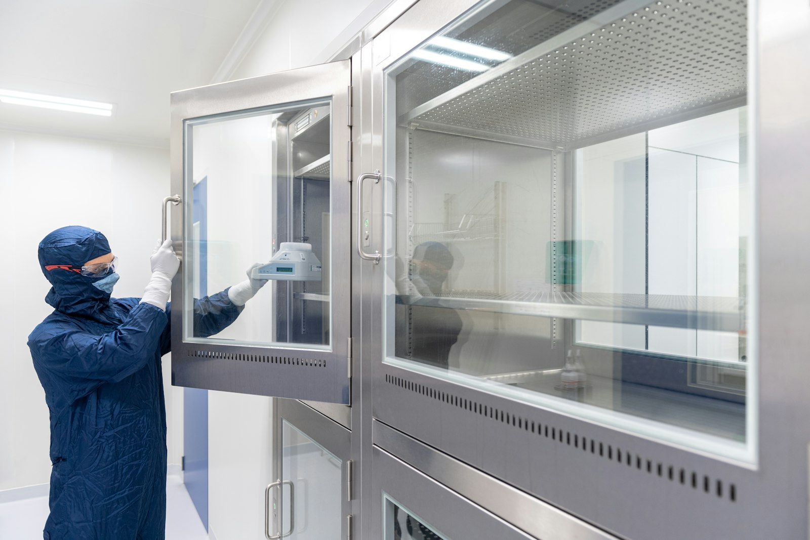 Gloved researcher in a cleanroom suit opening a stainless steel laboratory freezer